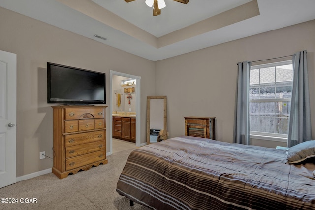 bedroom featuring a raised ceiling, ceiling fan, light colored carpet, and ensuite bathroom