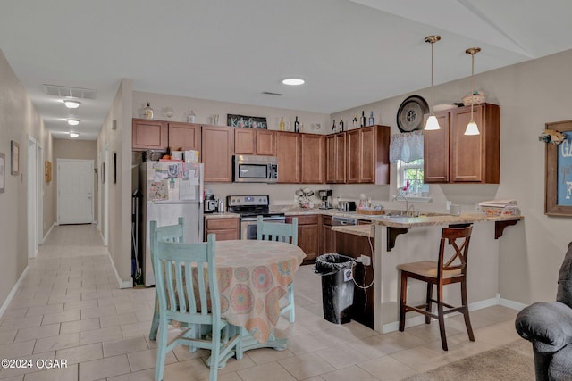 kitchen featuring light stone countertops, stainless steel appliances, kitchen peninsula, decorative light fixtures, and a breakfast bar area