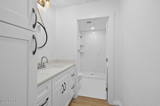 bathroom with hardwood / wood-style floors, vanity, toilet, and tiled shower