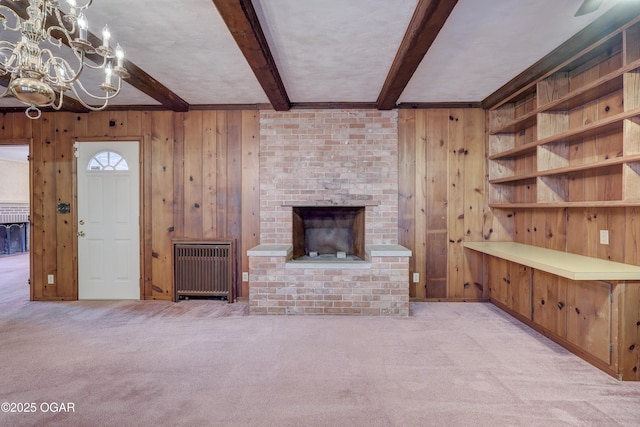 unfurnished living room featuring beam ceiling, light carpet, wooden walls, and a brick fireplace