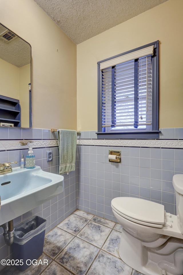 bathroom featuring tile patterned flooring, toilet, a textured ceiling, and tile walls