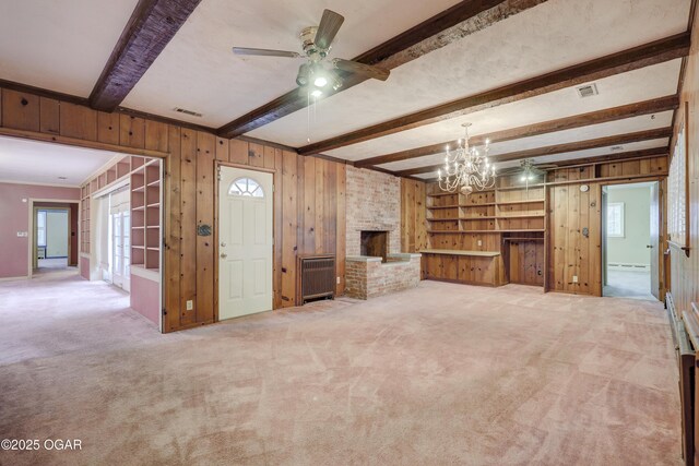 unfurnished living room with radiator, ceiling fan with notable chandelier, wooden walls, a fireplace, and beam ceiling