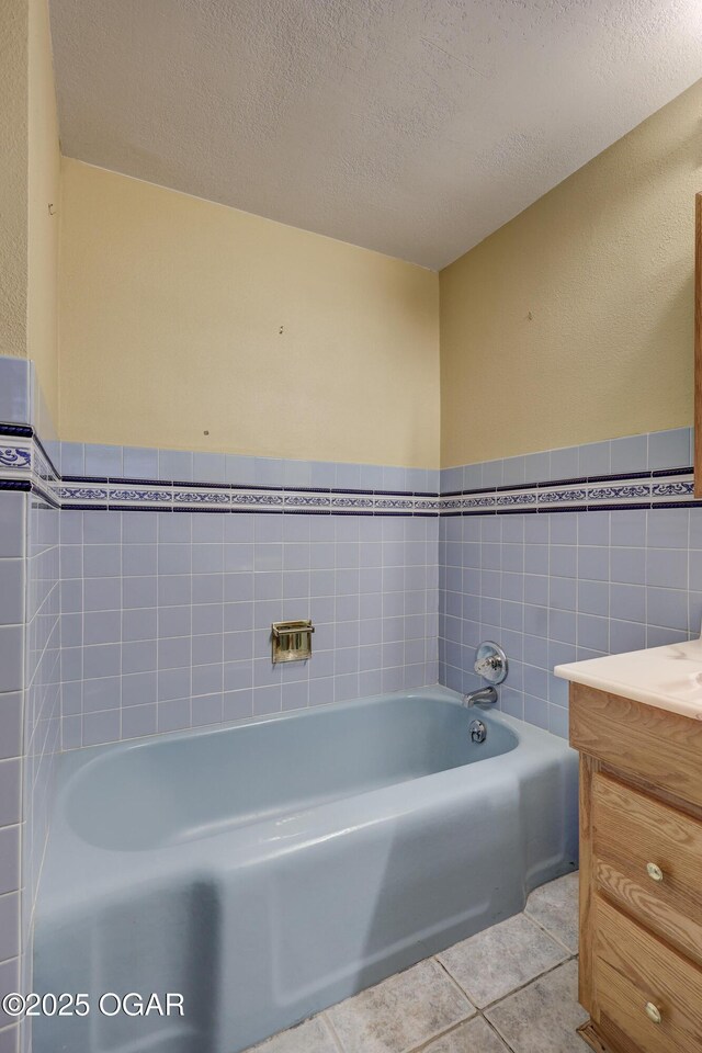 bathroom with vanity, a textured ceiling, tile walls, tile patterned flooring, and a bathing tub