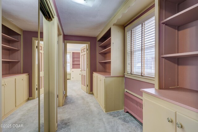 corridor featuring light carpet, built in features, and radiator