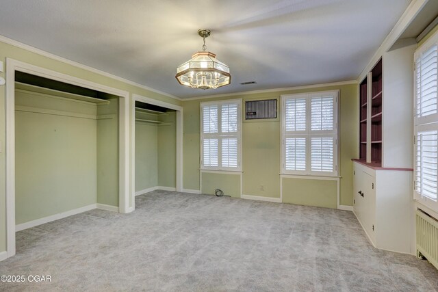 unfurnished bedroom featuring light carpet, radiator, an inviting chandelier, ornamental molding, and multiple closets