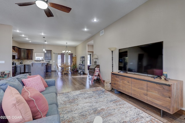 living room with ceiling fan with notable chandelier and dark hardwood / wood-style flooring