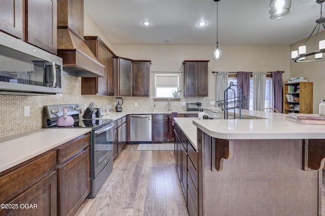 kitchen featuring custom exhaust hood, decorative light fixtures, a kitchen bar, dark brown cabinetry, and stainless steel appliances