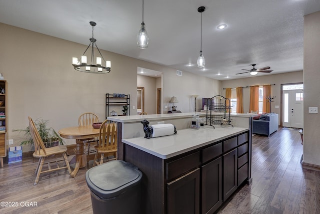 kitchen with ceiling fan with notable chandelier, decorative light fixtures, hardwood / wood-style flooring, dark brown cabinets, and a kitchen island