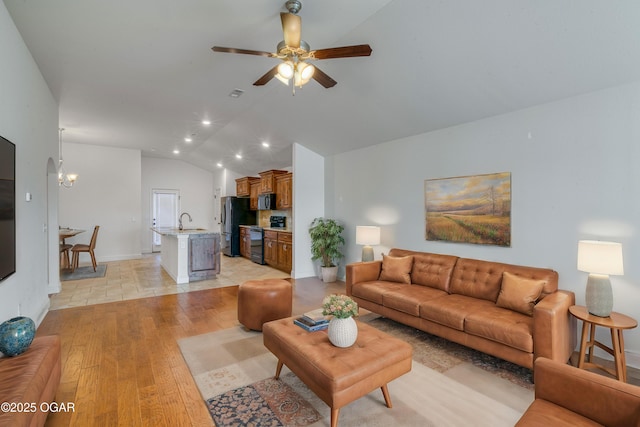 living room with ceiling fan with notable chandelier, light hardwood / wood-style floors, sink, and vaulted ceiling