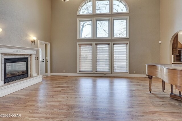 unfurnished living room with light hardwood / wood-style floors, a towering ceiling, and a tiled fireplace