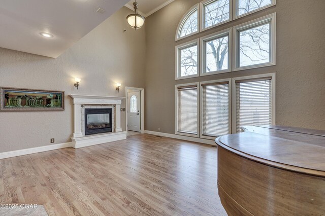 unfurnished living room with a tile fireplace, a high ceiling, light wood-type flooring, and crown molding