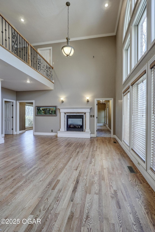 unfurnished living room featuring light hardwood / wood-style floors, a towering ceiling, and crown molding