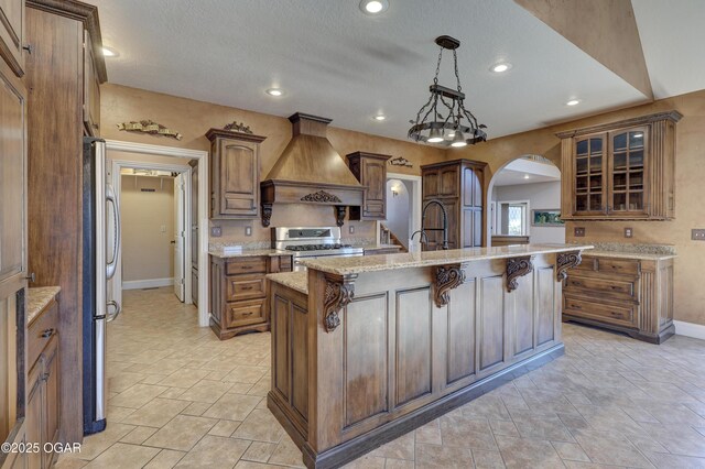 kitchen featuring premium range hood, a breakfast bar, stainless steel appliances, hanging light fixtures, and an island with sink