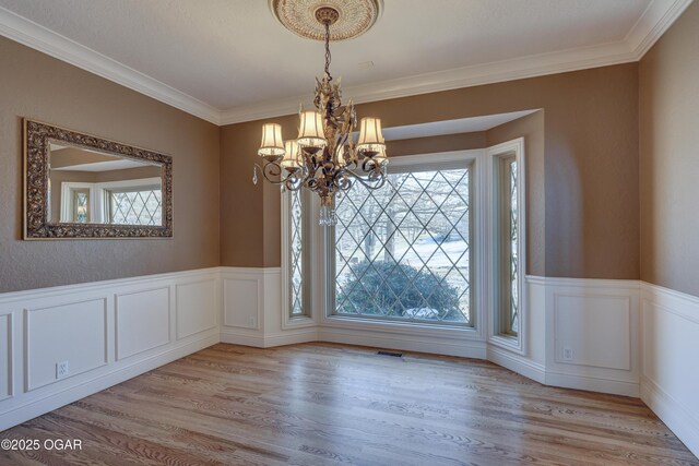 unfurnished dining area featuring a wealth of natural light, light hardwood / wood-style flooring, ornamental molding, and an inviting chandelier