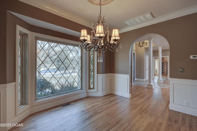 unfurnished dining area featuring decorative columns, crown molding, light hardwood / wood-style flooring, and a notable chandelier