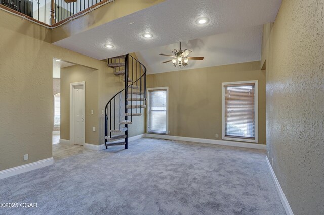 unfurnished living room with carpet flooring, a wealth of natural light, ceiling fan, and a textured ceiling