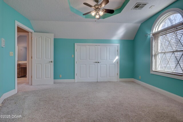 unfurnished bedroom featuring lofted ceiling, ceiling fan, a textured ceiling, light colored carpet, and a closet