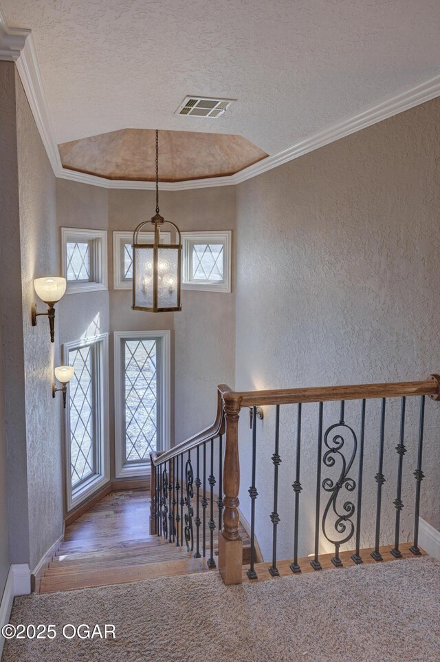 foyer entrance with crown molding, carpet floors, a textured ceiling, and an inviting chandelier