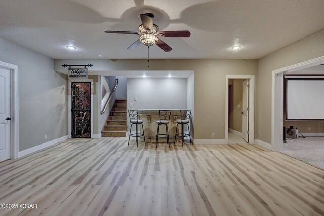 interior space with ceiling fan, light hardwood / wood-style floors, a textured ceiling, and indoor bar