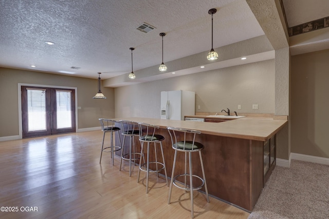 kitchen with kitchen peninsula, pendant lighting, white fridge with ice dispenser, and a kitchen breakfast bar