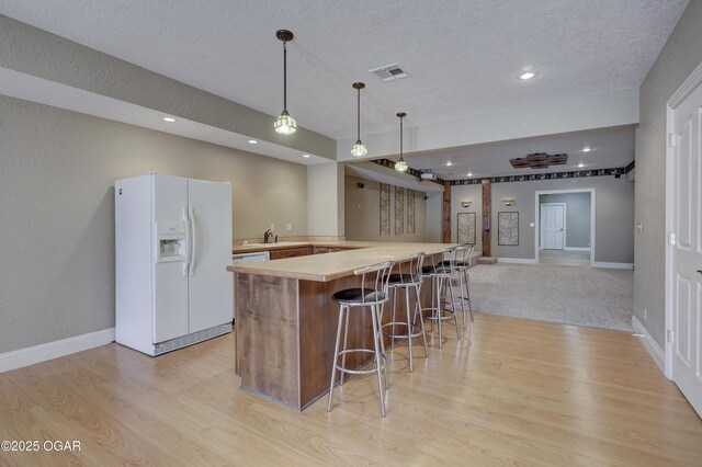 kitchen featuring a kitchen bar, a textured ceiling, hanging light fixtures, and white appliances