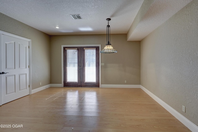 unfurnished dining area featuring french doors, light wood-type flooring, and a textured ceiling