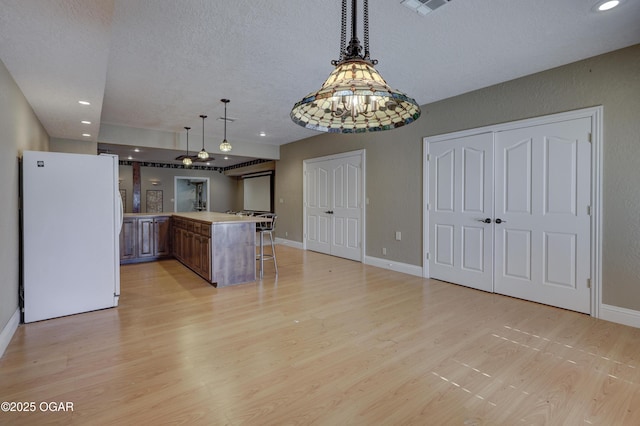 kitchen with pendant lighting, a kitchen breakfast bar, white fridge, and light hardwood / wood-style floors