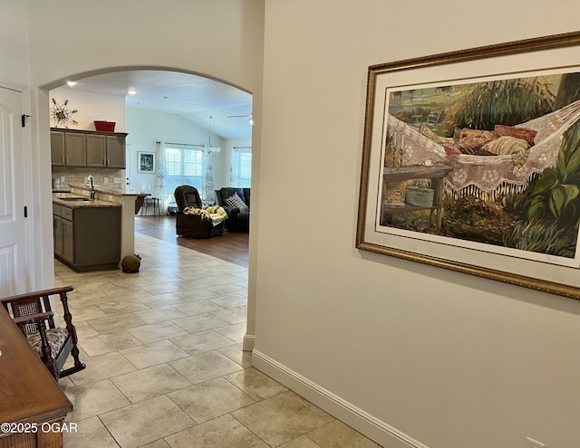 corridor featuring sink, light tile patterned floors, vaulted ceiling, and a notable chandelier