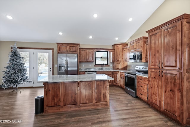 kitchen with light stone countertops, a center island, vaulted ceiling, and appliances with stainless steel finishes