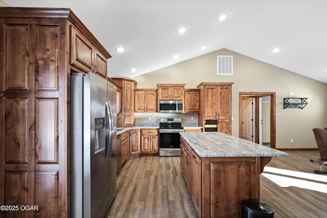 kitchen with a center island, vaulted ceiling, dark hardwood / wood-style floors, light stone countertops, and stainless steel appliances