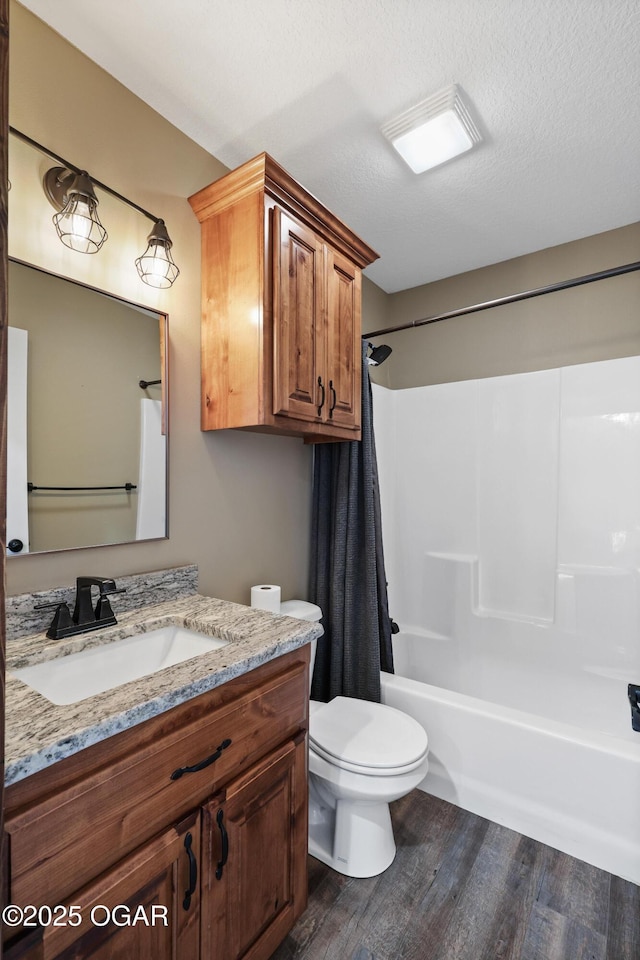 full bathroom with hardwood / wood-style floors, vanity, shower / bath combo, toilet, and a textured ceiling