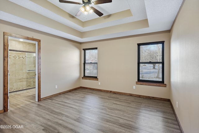 spare room with ceiling fan, a healthy amount of sunlight, light wood-type flooring, and a tray ceiling