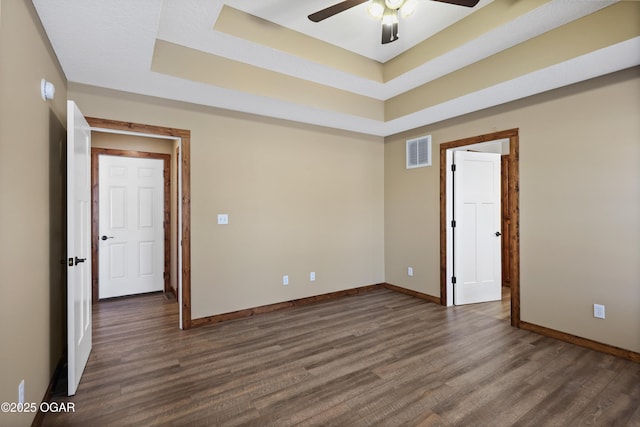 empty room with a raised ceiling, ceiling fan, and dark hardwood / wood-style flooring