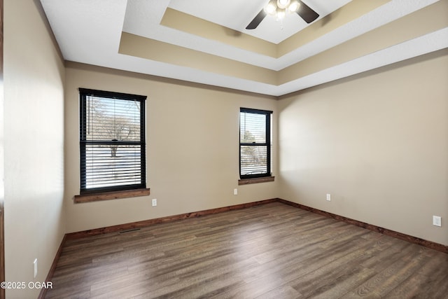 unfurnished room featuring a tray ceiling, plenty of natural light, and dark wood-type flooring