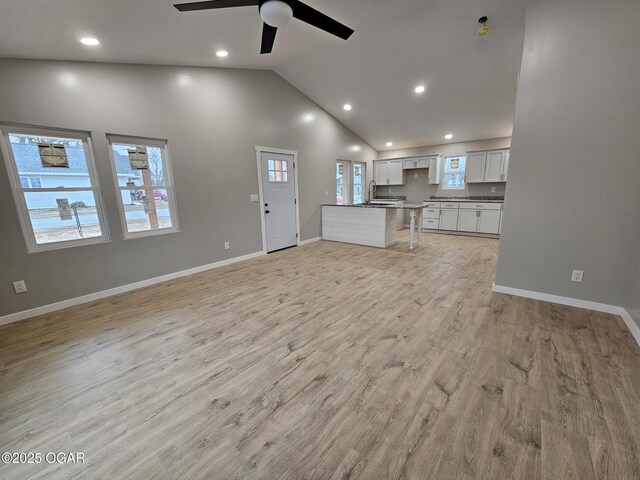 unfurnished living room with sink, light hardwood / wood-style flooring, high vaulted ceiling, and ceiling fan