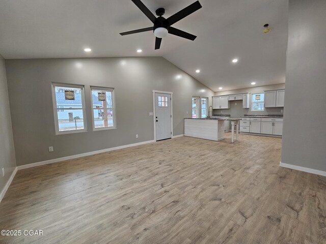 unfurnished living room featuring high vaulted ceiling, sink, ceiling fan, and light hardwood / wood-style flooring