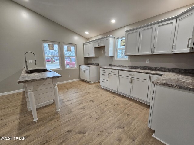 kitchen with vaulted ceiling, sink, white cabinets, dark stone counters, and light wood-type flooring