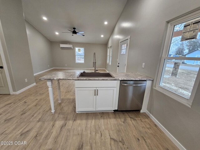 kitchen featuring white cabinetry, sink, light wood-type flooring, stainless steel dishwasher, and a wall unit AC