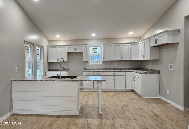 kitchen featuring lofted ceiling, sink, white cabinetry, light wood-type flooring, and dark stone counters