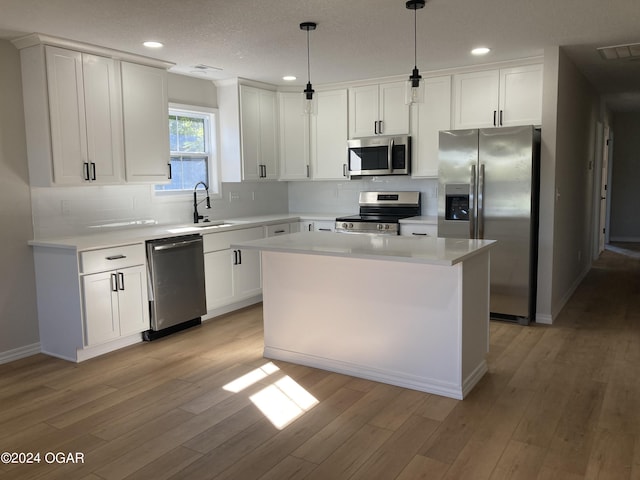 kitchen with sink, hanging light fixtures, stainless steel appliances, light hardwood / wood-style flooring, and white cabinets