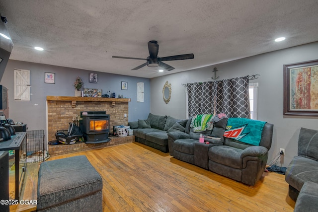 living room featuring a textured ceiling, hardwood / wood-style flooring, a wood stove, and ceiling fan