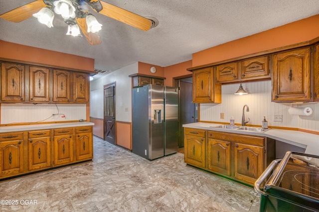 kitchen with sink, stainless steel fridge, stove, ceiling fan, and a textured ceiling