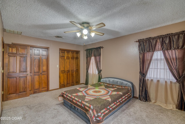 carpeted bedroom featuring multiple closets, a textured ceiling, and ceiling fan