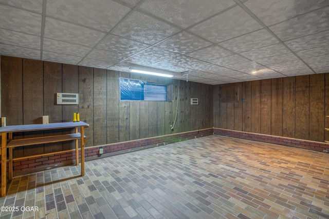 basement featuring a drop ceiling and wood walls