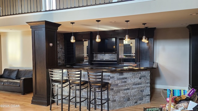 bar featuring backsplash, decorative light fixtures, decorative columns, and light wood-type flooring