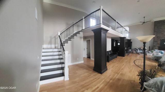 staircase with a high ceiling, ornamental molding, hardwood / wood-style floors, and decorative columns