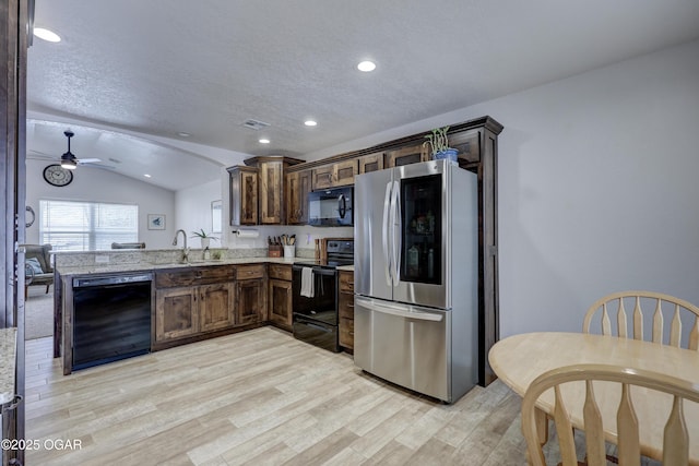 kitchen with lofted ceiling, kitchen peninsula, light stone countertops, dark brown cabinetry, and black appliances