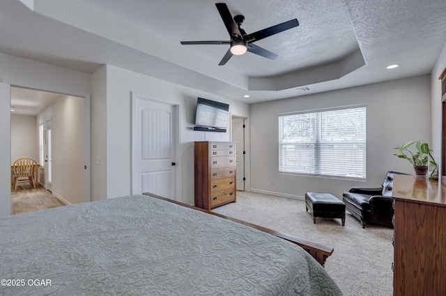 carpeted bedroom with ceiling fan, a textured ceiling, and a tray ceiling