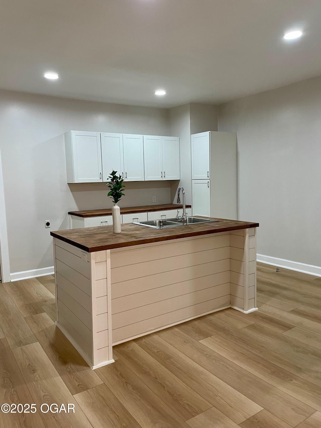 kitchen with butcher block counters, a sink, a kitchen island with sink, and white cabinets