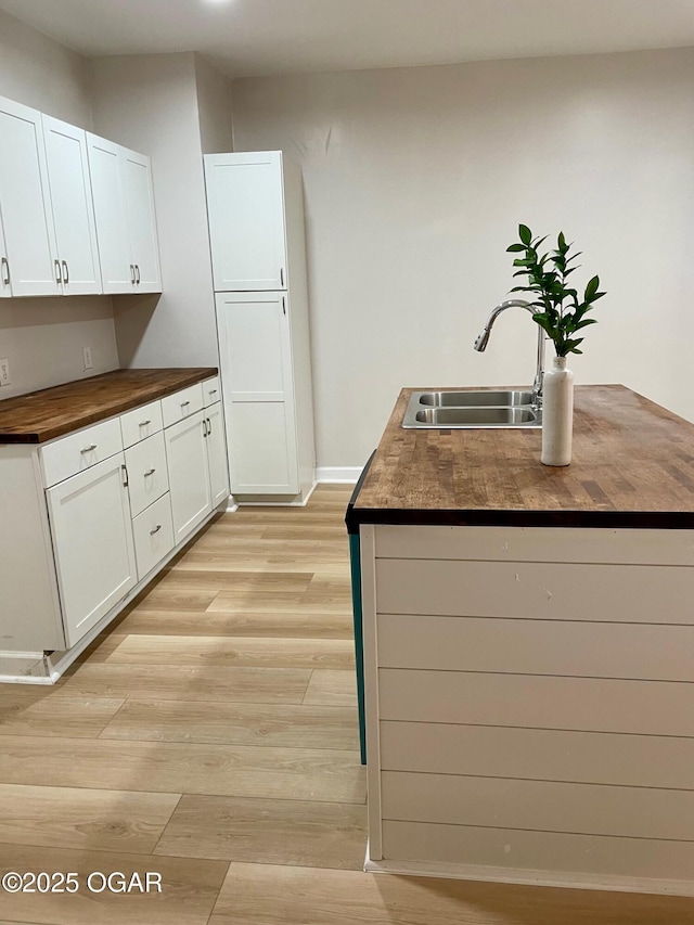 kitchen with white cabinets, a sink, wood counters, and light wood finished floors